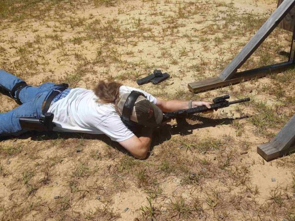 A person aiming with a gun while lying on ground